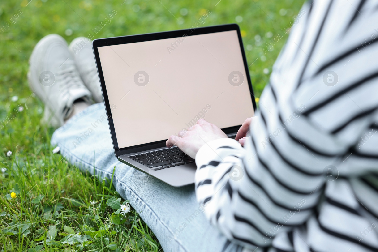 Photo of Freelancer working with laptop on green grass outdoors, closeup. Remote job