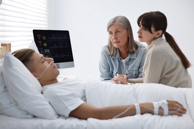 Photo of Coma patient. Sad women near unconscious young man in hospital