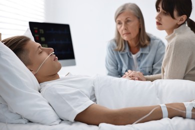 Coma patient. Sad women near unconscious young man in hospital