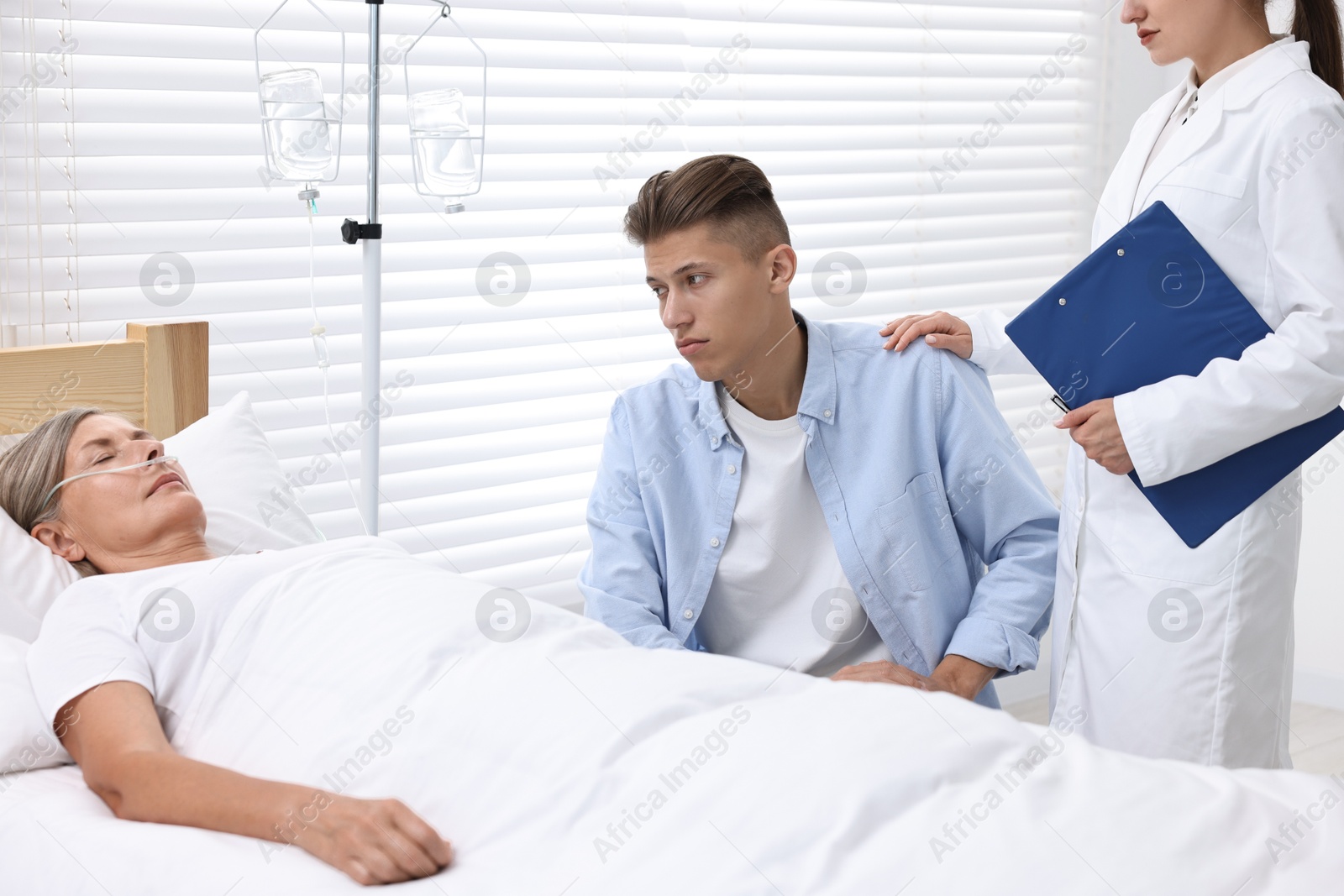 Photo of Coma patient. Sad young man near his unconscious mother talking with doctor in hospital