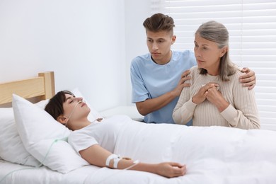 Coma patient. Sad relatives near sleeping young woman in hospital