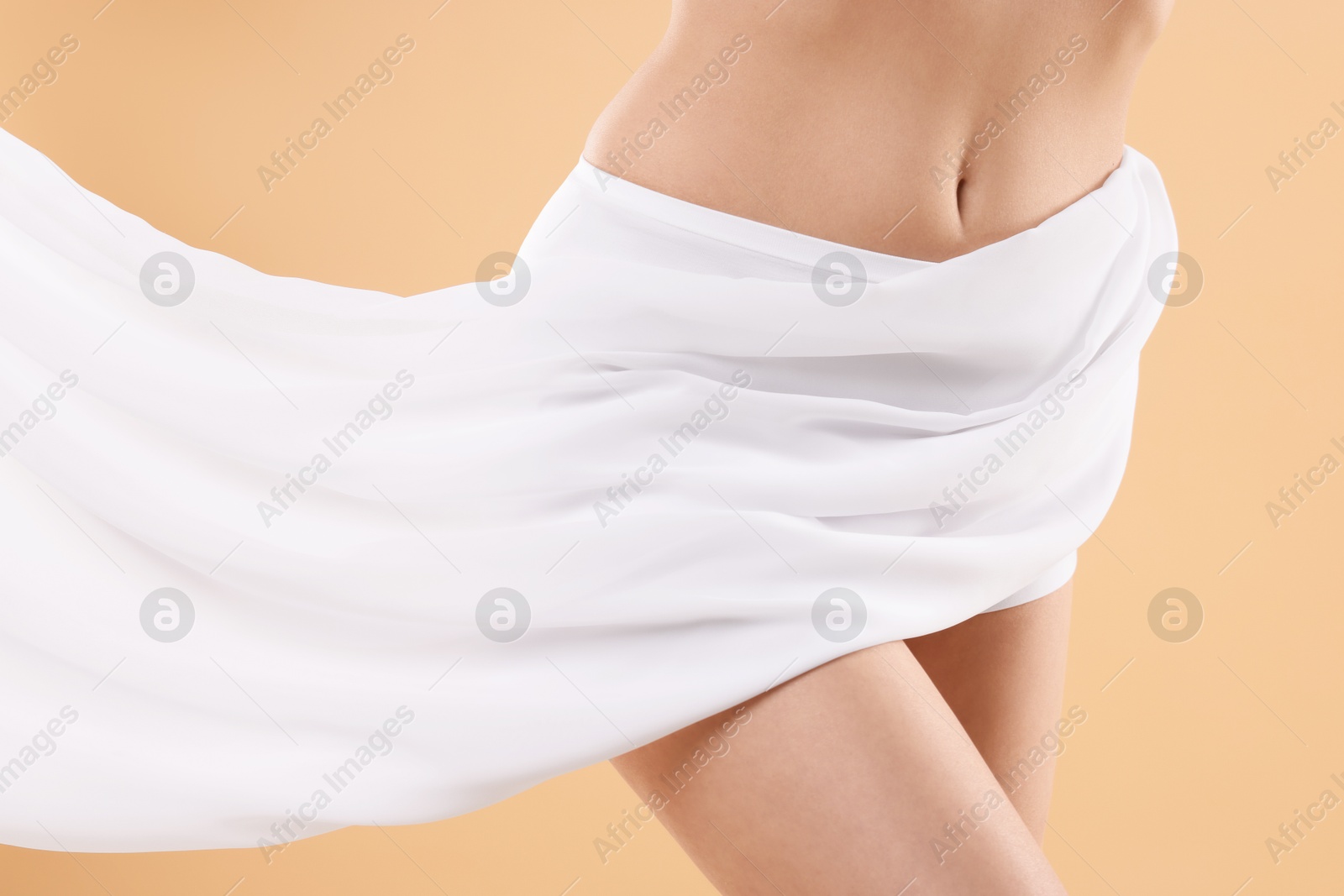 Photo of Diet and weight loss concept. Woman covering her slim body with silk fabric against beige background, closeup