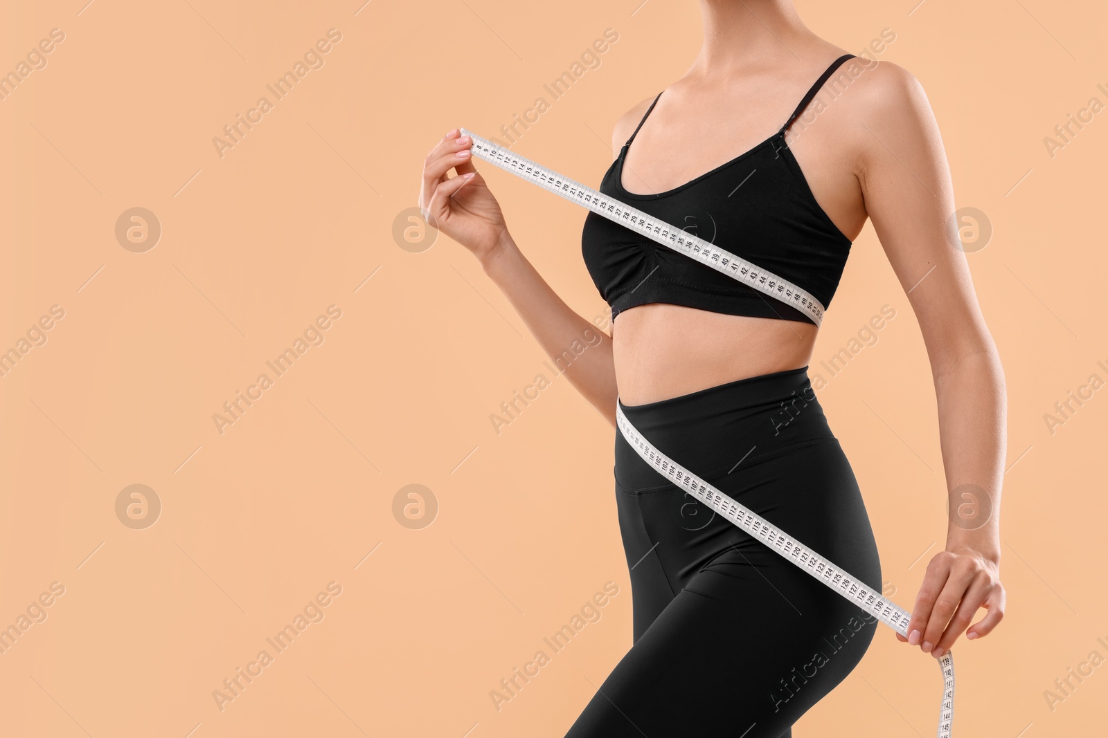 Photo of Diet and weight loss concept. Woman with measuring tape showing her slim body against beige background, closeup. Space for text