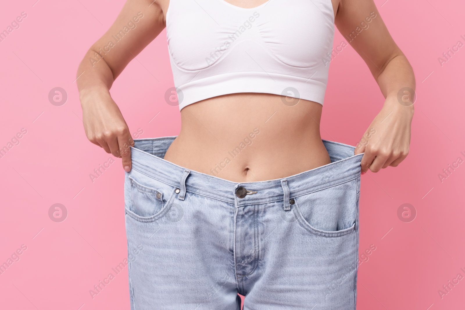 Photo of Diet and weight loss concept. Woman in big jeans showing her slim body on pink background, closeup