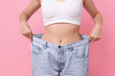 Diet and weight loss concept. Woman in big jeans showing her slim body on pink background, closeup