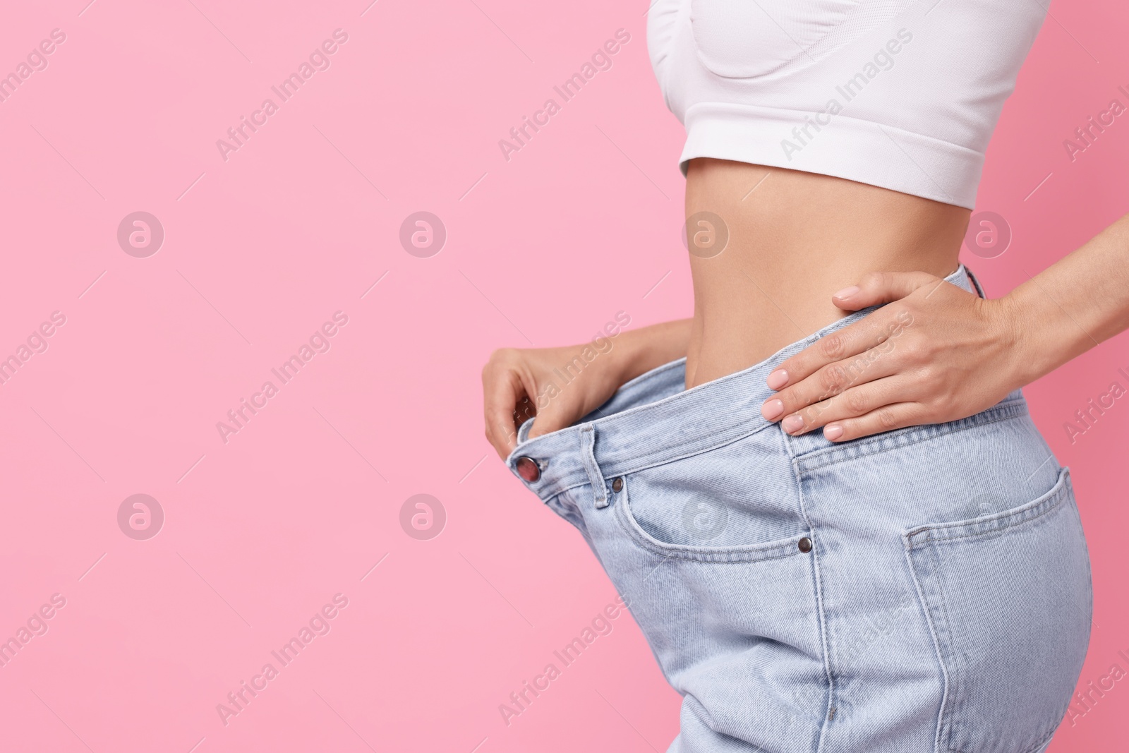 Photo of Diet and weight loss concept. Woman in big jeans showing her slim body on pink background, closeup. Space for text