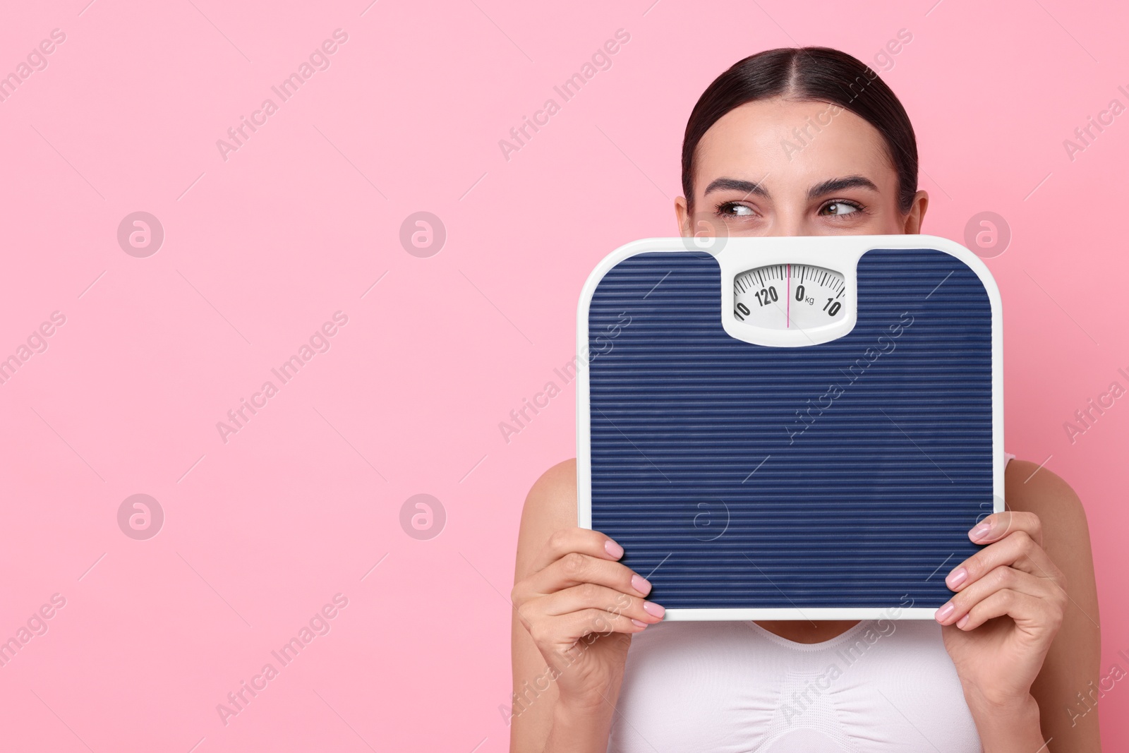 Photo of Diet and weight loss concept. Young woman with floor scale on pink background. Space for text