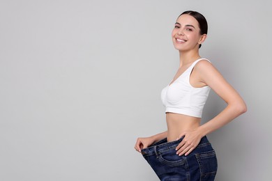 Photo of Diet and weight loss concept. Happy young woman in big jeans showing her slim body on light grey background. Space for text