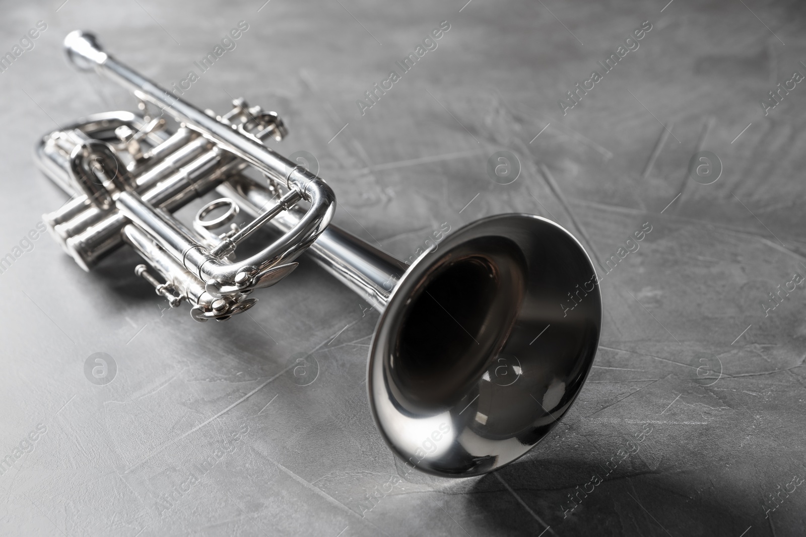 Photo of Closeup view of shiny trumpet on grey textured table. Wind musical instrument