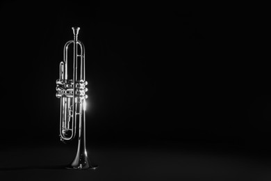 Shiny trumpet on black background, space for text. Wind musical instrument