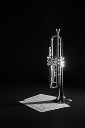 Shiny trumpet and music sheets on dark background. Wind musical instrument