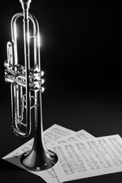 Photo of Shiny trumpet and music sheets on dark background. Wind musical instrument