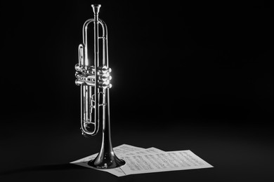 Shiny trumpet and music sheets on dark background, space for text. Wind musical instrument