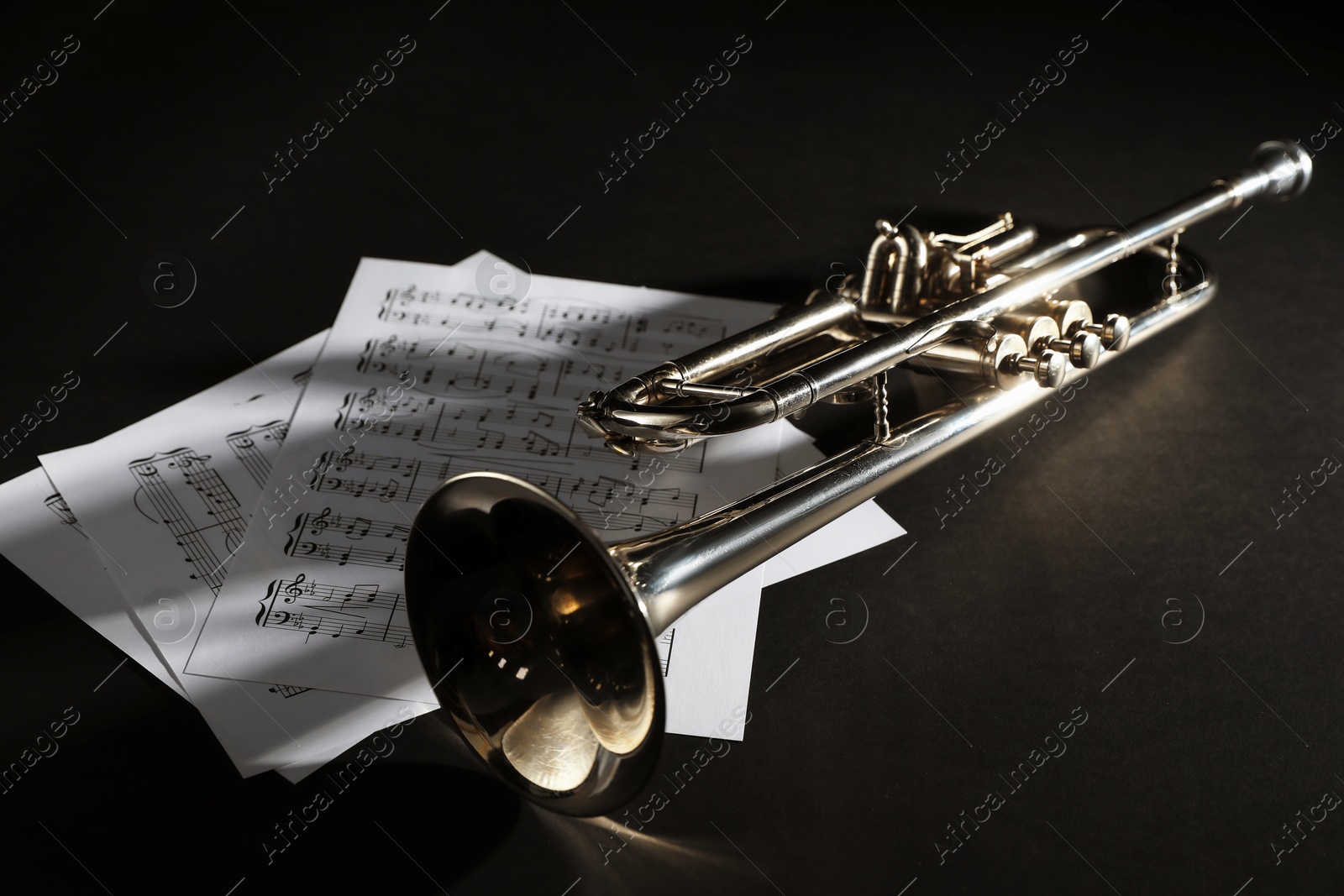 Photo of Shiny trumpet and music sheets on dark background. Wind musical instrument