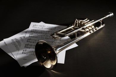 Shiny trumpet and music sheets on dark background. Wind musical instrument