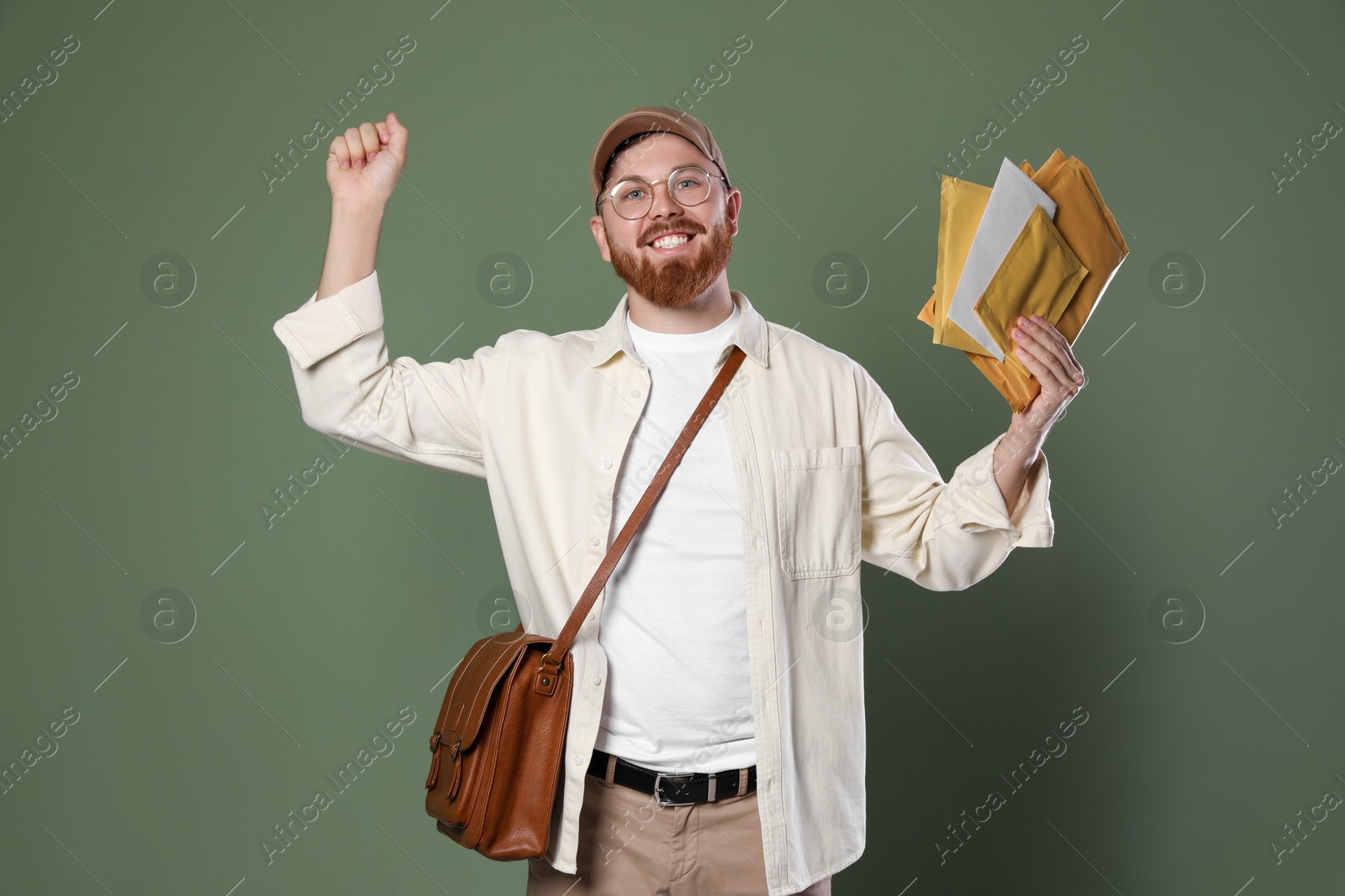 Photo of Happy young postman with brown bag delivering letters on olive background