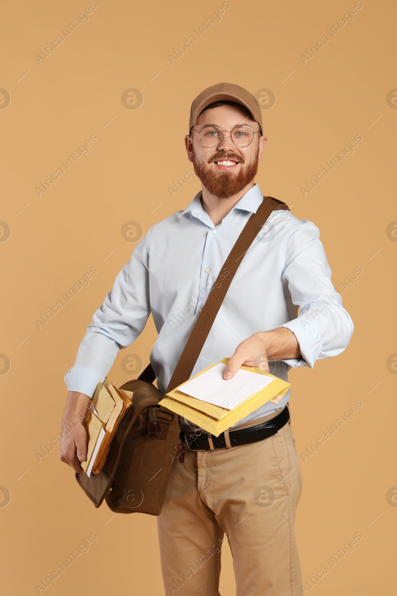 Photo of Happy young postman with leather bag delivering letters on brown background