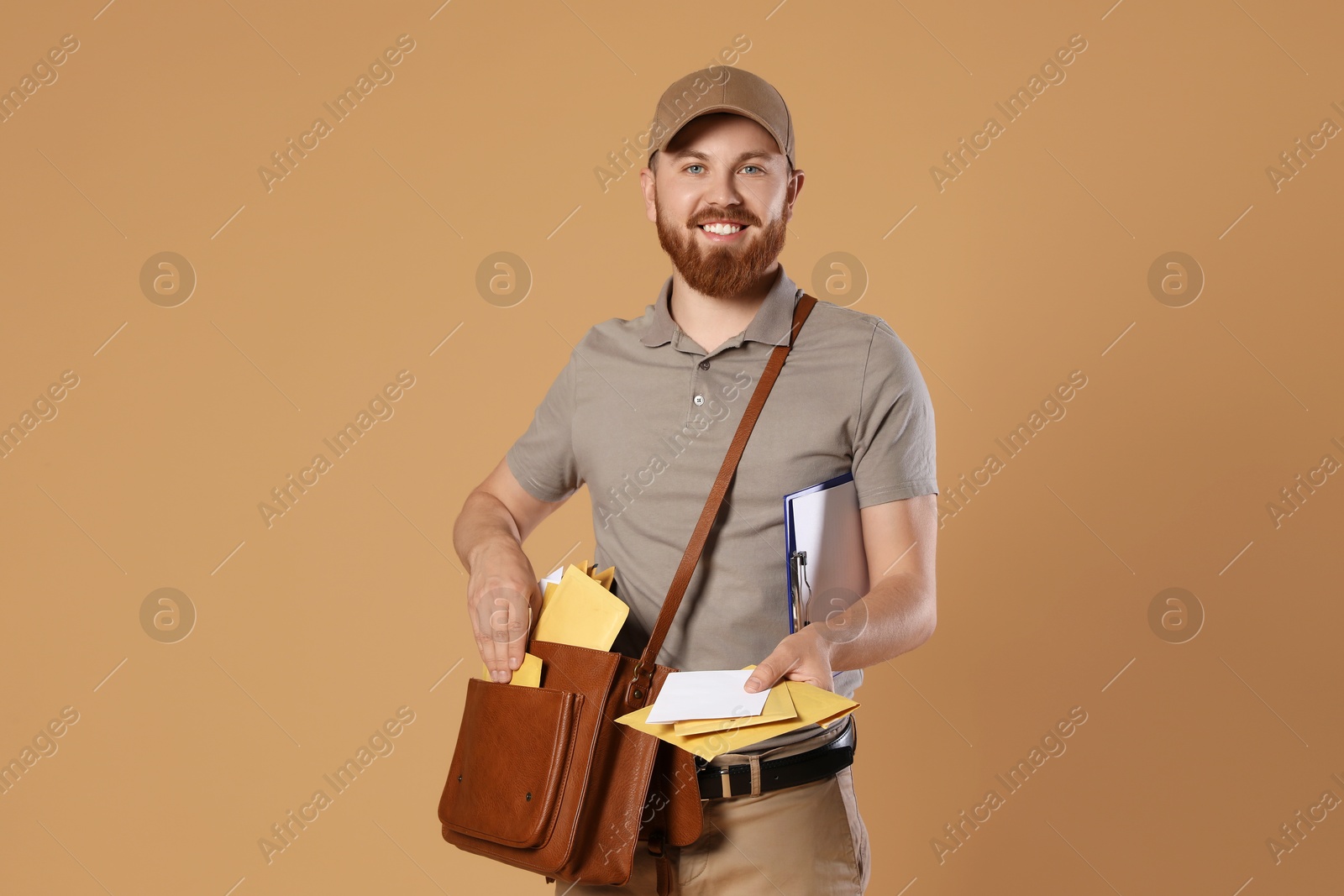 Photo of Happy young postman with leather bag delivering letters on brown background. Space for text