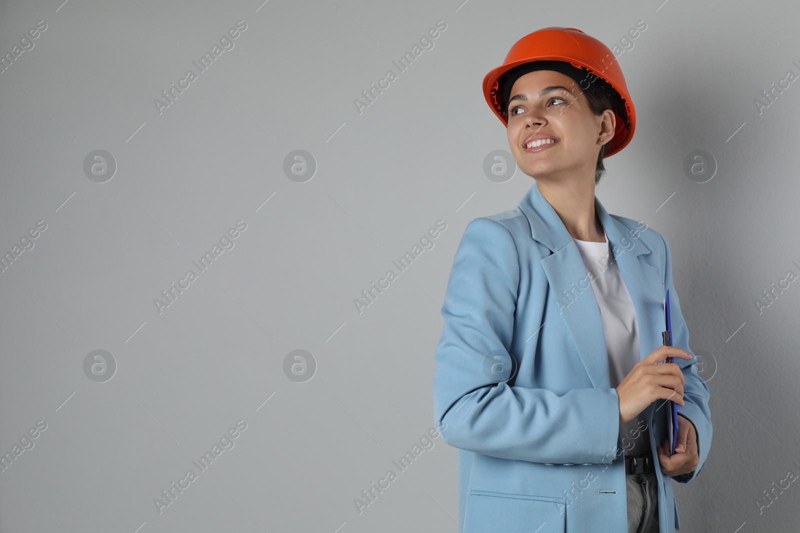 Photo of Engineer in hard hat with clipboard on grey background, space for text