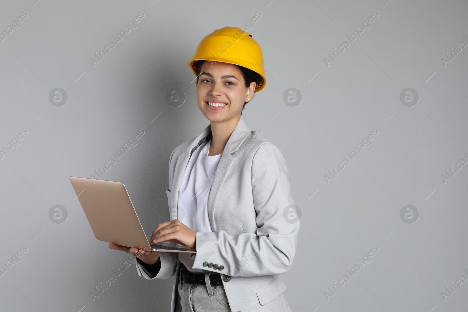 Photo of Engineer in hard hat with laptop on grey background, space for text