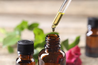 Photo of Essential oil dripping from pipette into bottle at table, closeup