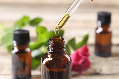 Photo of Essential oil dripping from pipette into bottle at table, closeup