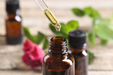 Photo of Essential oil dripping from pipette into bottle at table, closeup