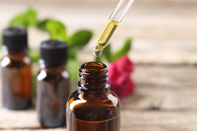 Photo of Essential oil dripping from pipette into bottle at table, closeup