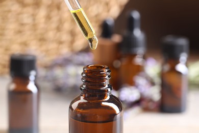 Photo of Essential oil dripping from pipette into bottle at table, closeup