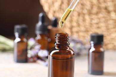 Photo of Essential oil dripping from pipette into bottle at table, closeup