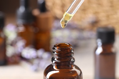 Photo of Essential oil dripping from pipette into bottle against blurred background, closeup