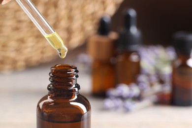 Essential oil dripping from pipette into bottle against blurred background, closeup. Space for text