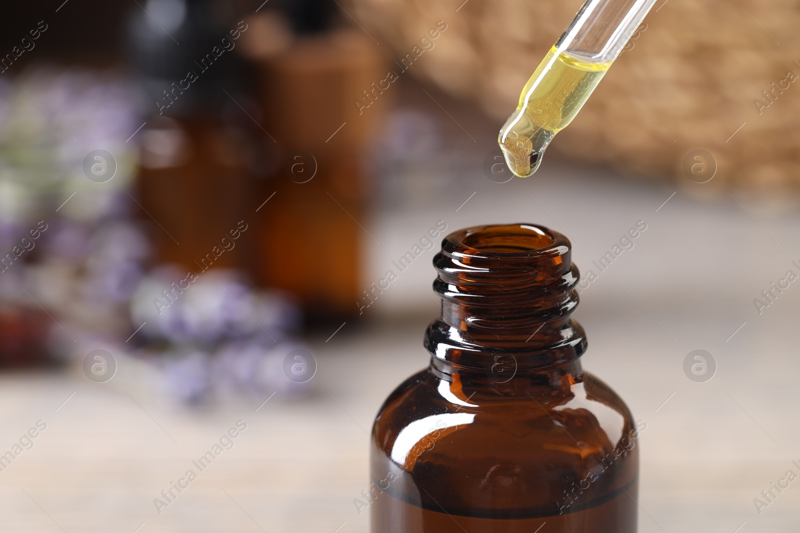 Photo of Essential oil dripping from pipette into bottle against blurred background, closeup