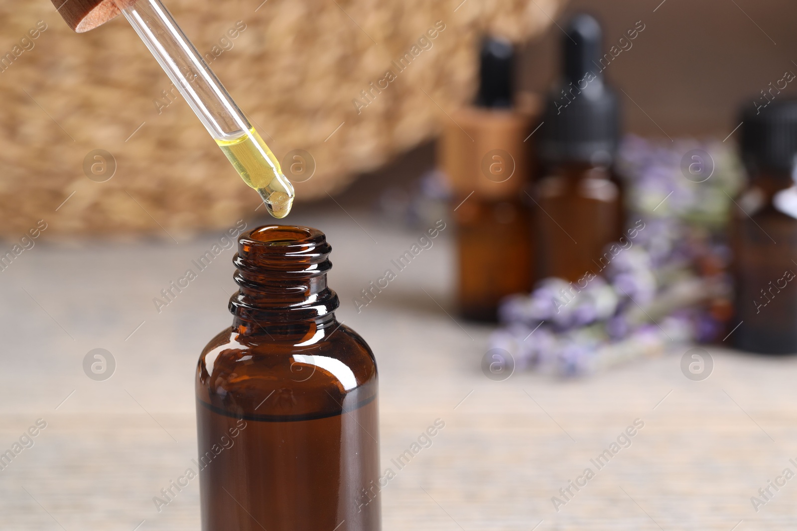 Photo of Essential oil dripping from pipette into bottle at table, closeup. Space for text