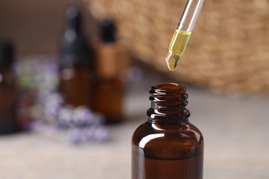 Photo of Essential oil dripping from pipette into bottle against blurred background, closeup