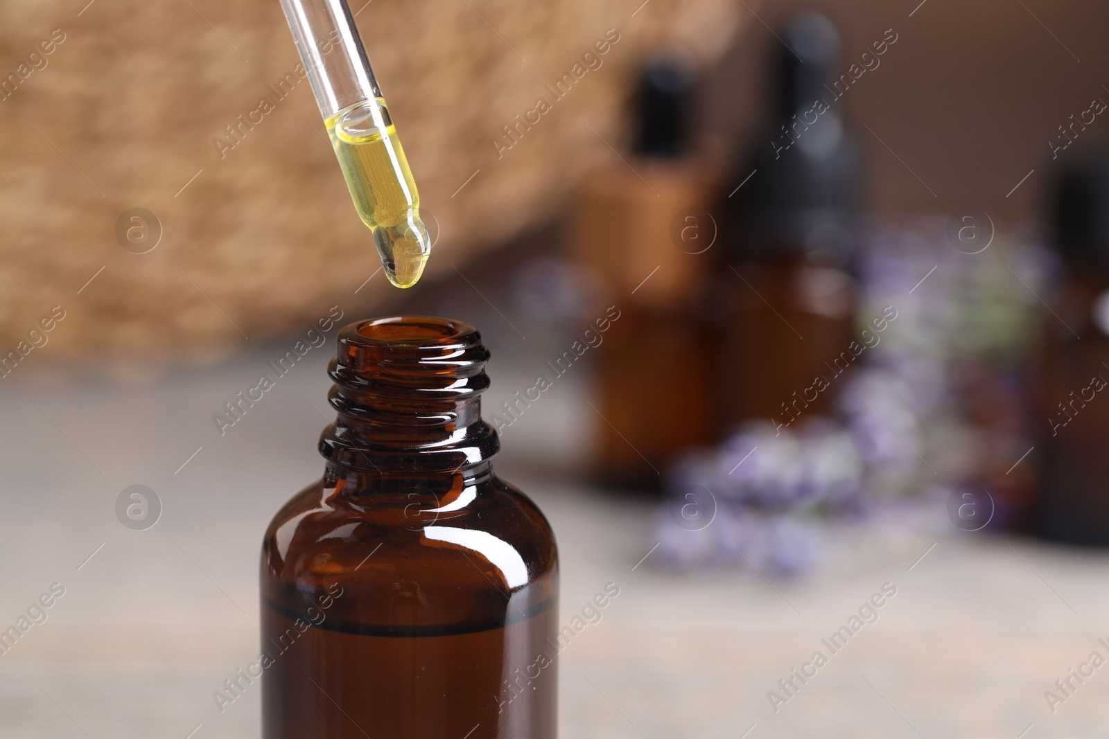 Photo of Essential oil dripping from pipette into bottle against blurred background, closeup. Space for text