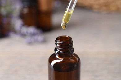 Photo of Essential oil dripping from pipette into bottle against blurred background, closeup