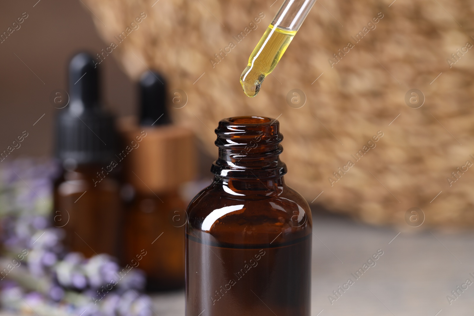 Photo of Essential oil dripping from pipette into bottle at table, closeup