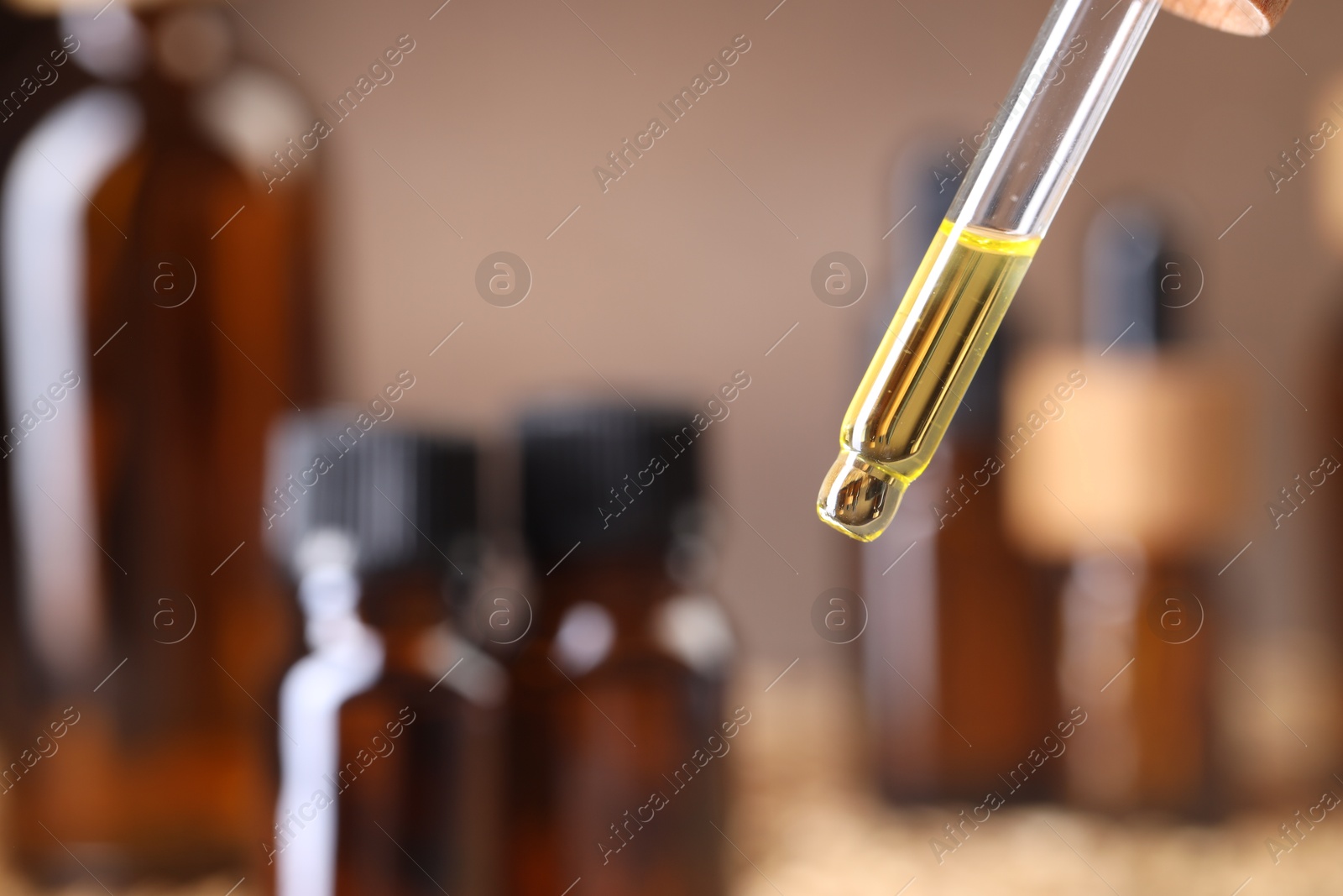 Photo of Essential oil dripping from pipette against blurred background, closeup. Space for text