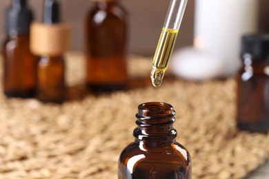 Photo of Essential oil dripping from pipette into bottle at table, closeup