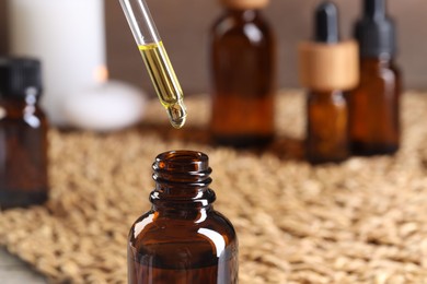 Photo of Essential oil dripping from pipette into bottle at table, closeup