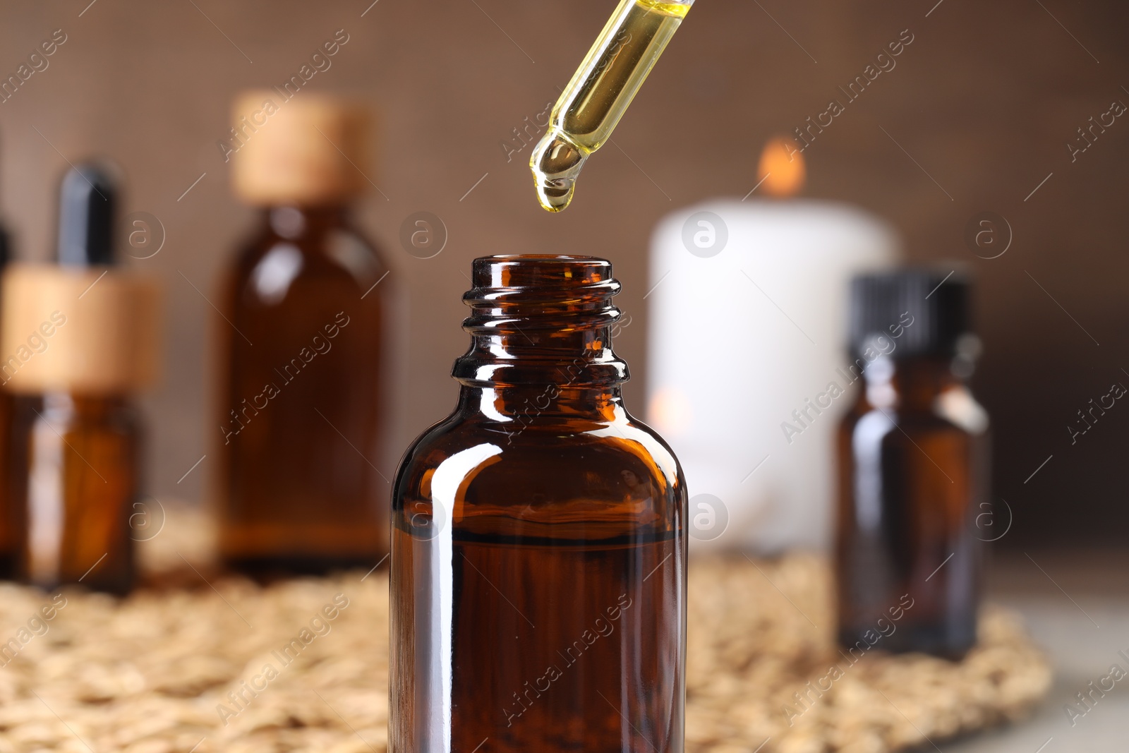 Photo of Essential oil dripping from pipette into bottle at table, closeup