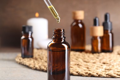 Photo of Essential oil dripping from pipette into bottle at table, closeup