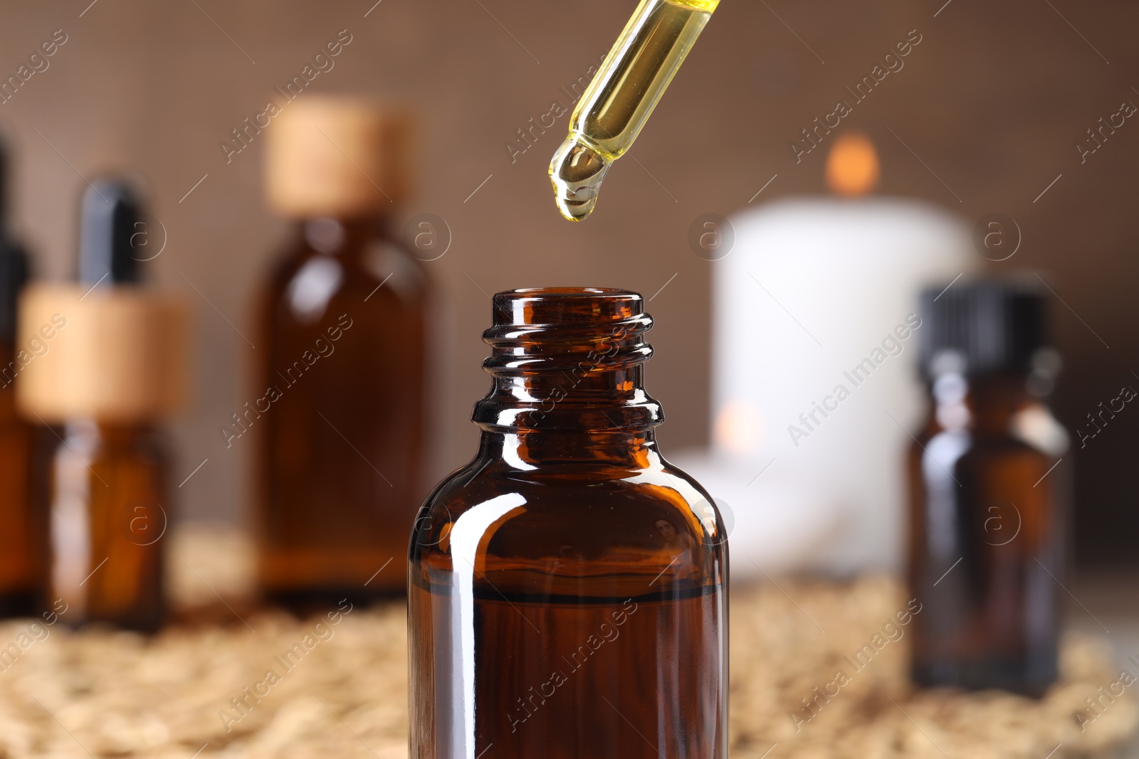 Photo of Essential oil dripping from pipette into bottle at table, closeup