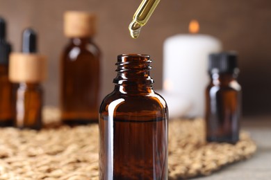 Photo of Essential oil dripping from pipette into bottle at table, closeup