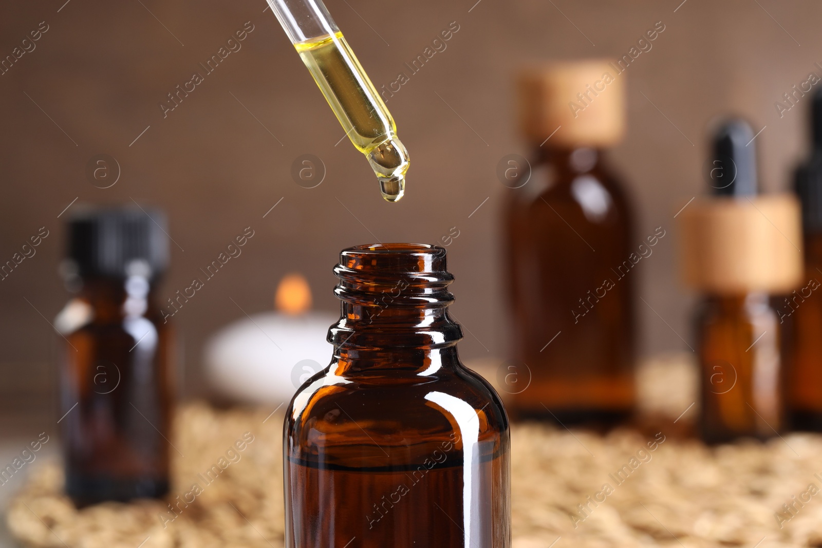 Photo of Essential oil dripping from pipette into bottle at table, closeup