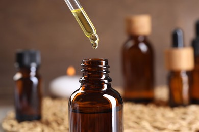 Photo of Essential oil dripping from pipette into bottle at table, closeup