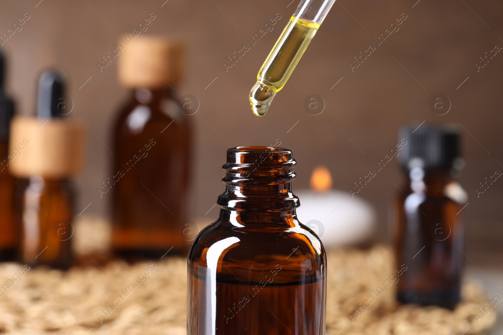 Photo of Essential oil dripping from pipette into bottle at table, closeup