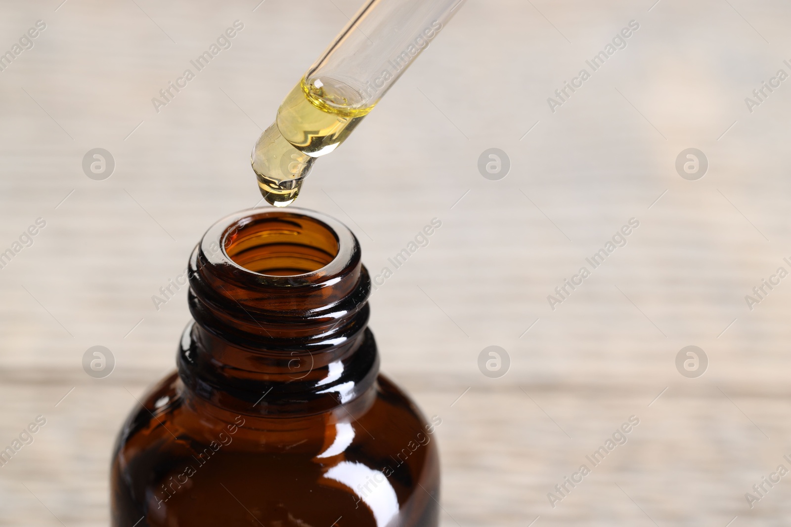 Photo of Essential oil dripping from pipette into bottle against blurred background, closeup. Space for text