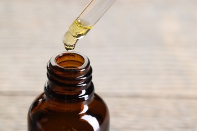 Photo of Essential oil dripping from pipette into bottle against blurred background, closeup. Space for text